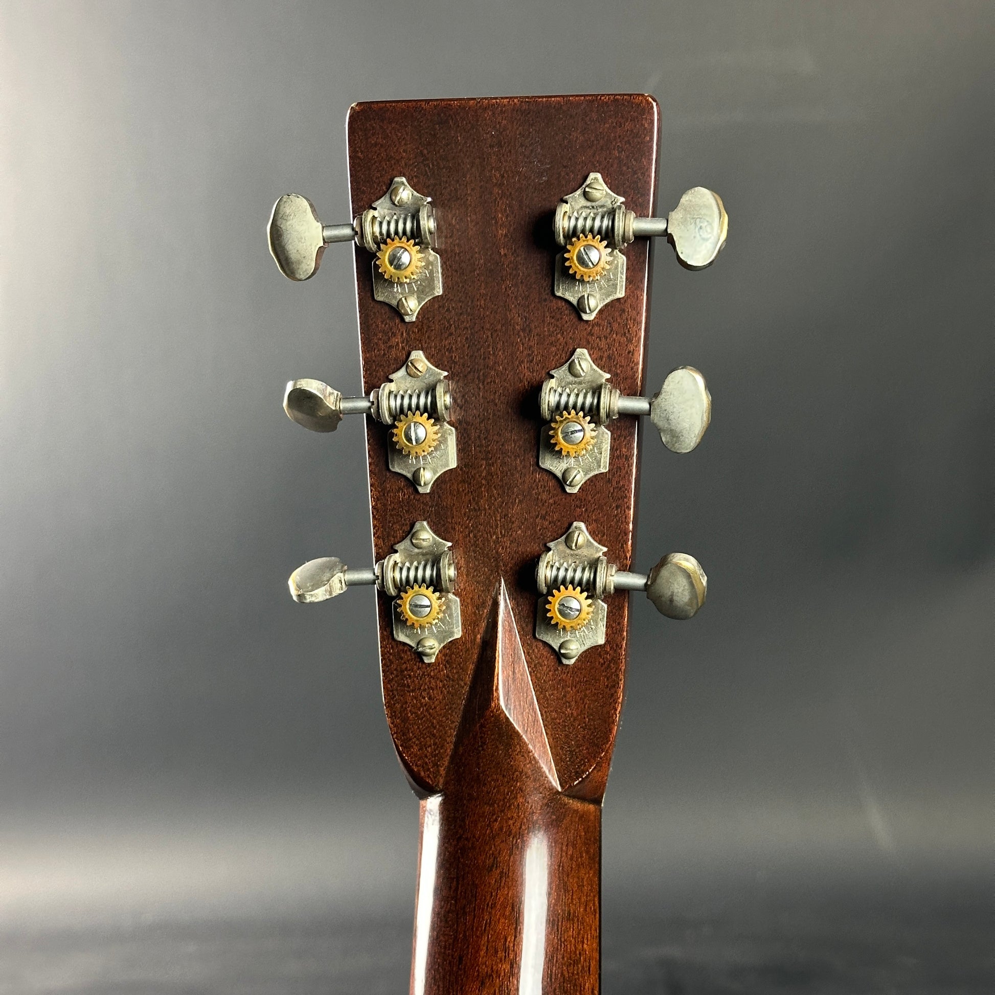 Close-up of a guitar headstock with tuning pegs on a gray background