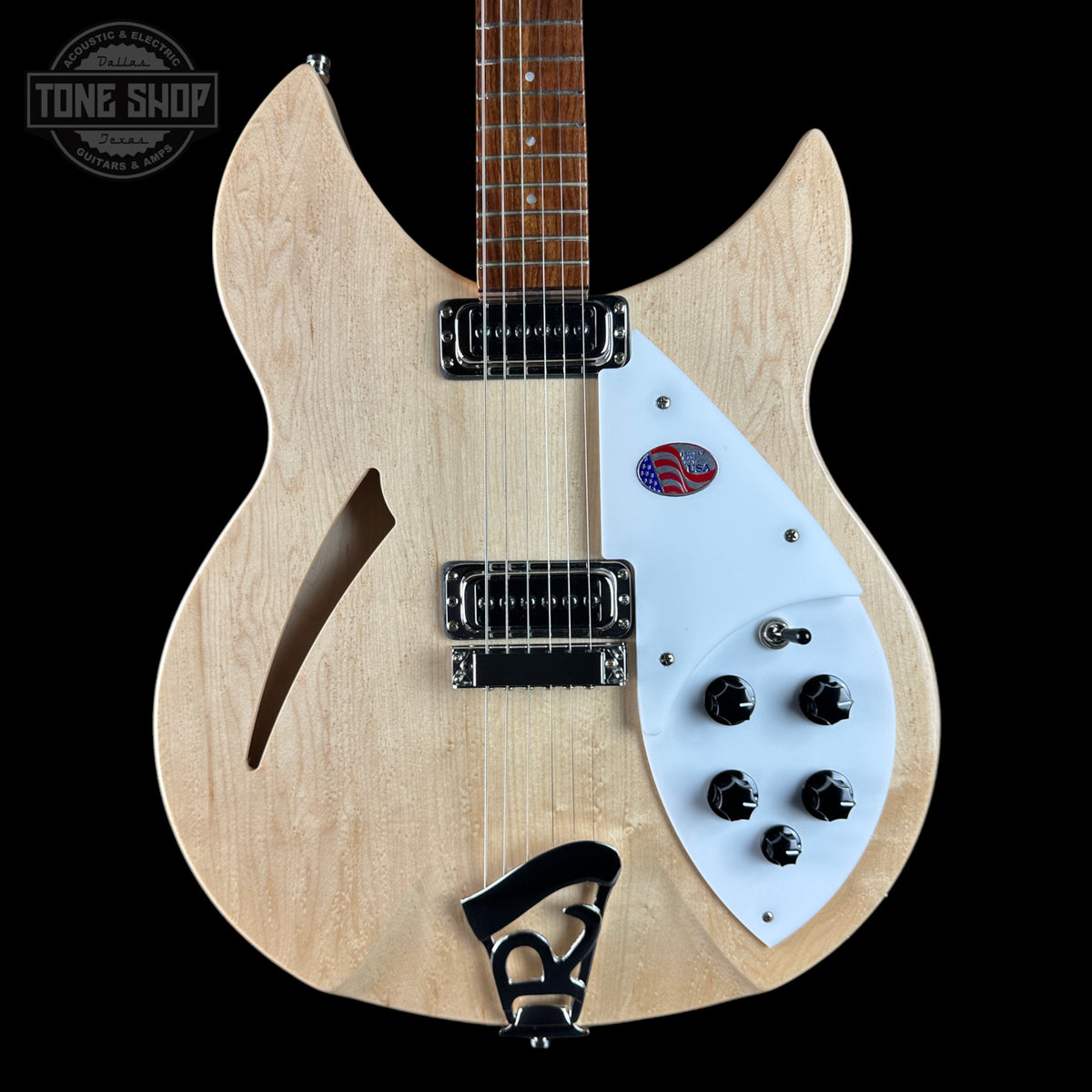 A double-cutaway electric guitar with a natural wood body, white pickguard, and black hardware, shown against a solid black background. A Tone Shop watermark is visible in the top left corner.