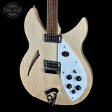 A double-cutaway electric guitar with a natural wood finish body, a white pickguard, and black hardware, shown against a solid black background. A Tone Shop watermark is visible in the top-left corner.