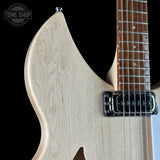 Close-up of an electric guitar body showing a light natural wood finish, chrome hardware, and part of the dark fretboard against a black background. A Tone Shop watermark is visible in the upper left.
