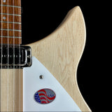 Close-up of a guitar body showing a light natural wood finish, a white pickguard with a small oval American flag emblem, and part of the fretboard against a black background.
