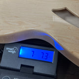 A close-up of a light natural wood guitar body resting on a digital smart scale displaying a weight of 7.73 kg.