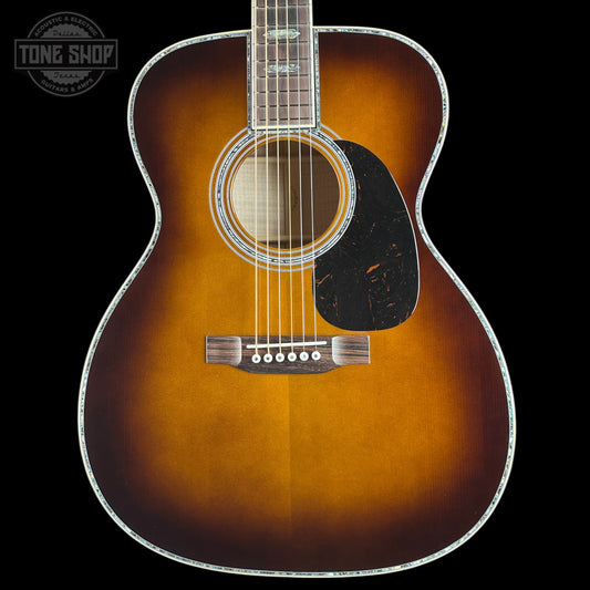 A classic acoustic guitar with a sunburst finish, featuring a dark brown outer edge fading to a warm amber-orange center, set against a solid black background.