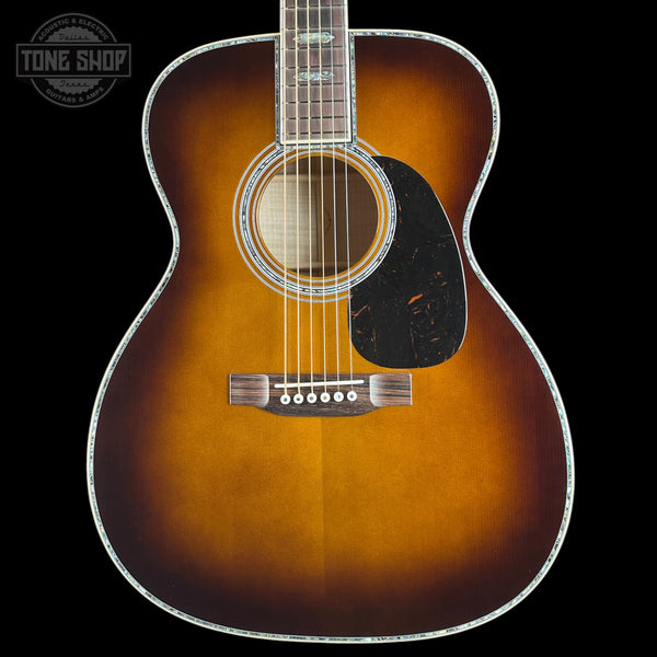 A classic acoustic guitar with a sunburst finish, featuring a dark brown outer edge fading to a warm amber-orange center, set against a solid black background.
