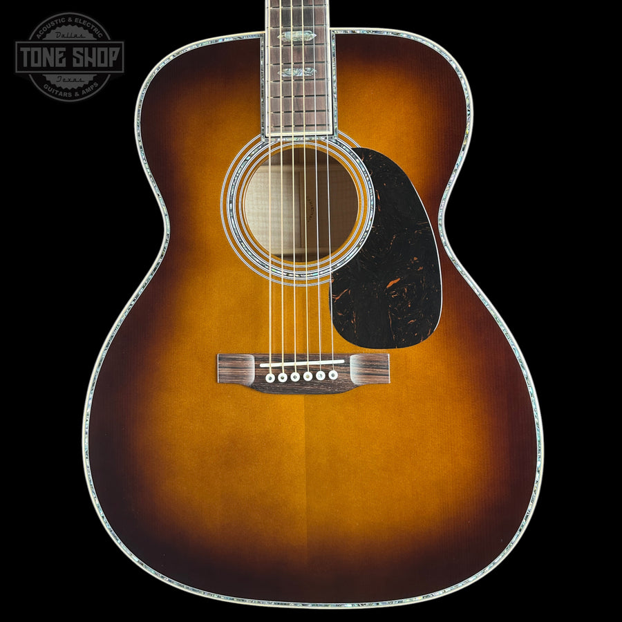 A classic acoustic guitar with a sunburst finish, featuring a dark brown outer edge fading to a warm amber-orange center, set against a solid black background.
