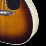 Close-up detail of an acoustic guitar body showing the sunburst finish, pickguard, bridge, and fluted edge against a black background.