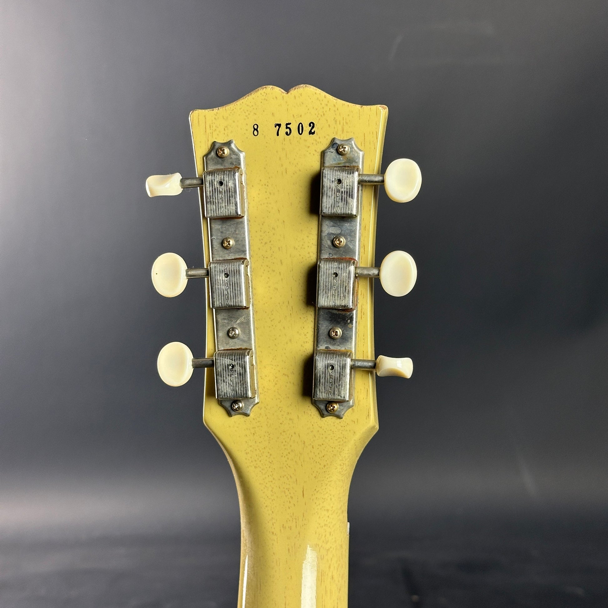 Close-up of a guitar headstock with tuning pegs on a dark background