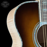 Close-up of an acoustic guitar body showing the natural wood outer edge, dark brown sunburst finish, and decorative inlay around the soundhole and neck, on a black background with a Tone Shop watermark.