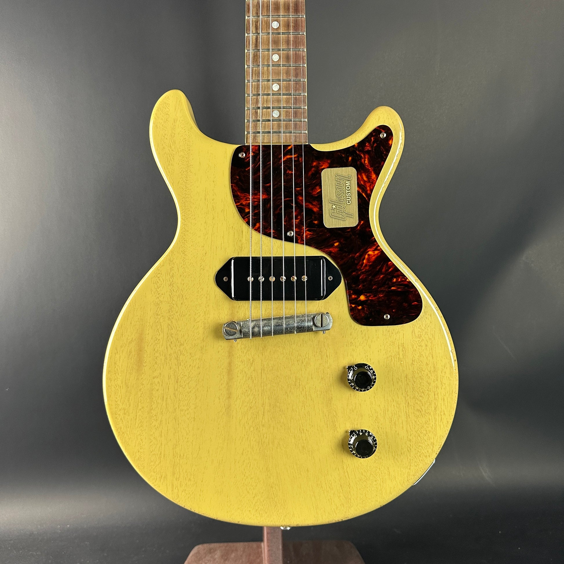 Yellow electric guitar with a dark fretboard on a gray background