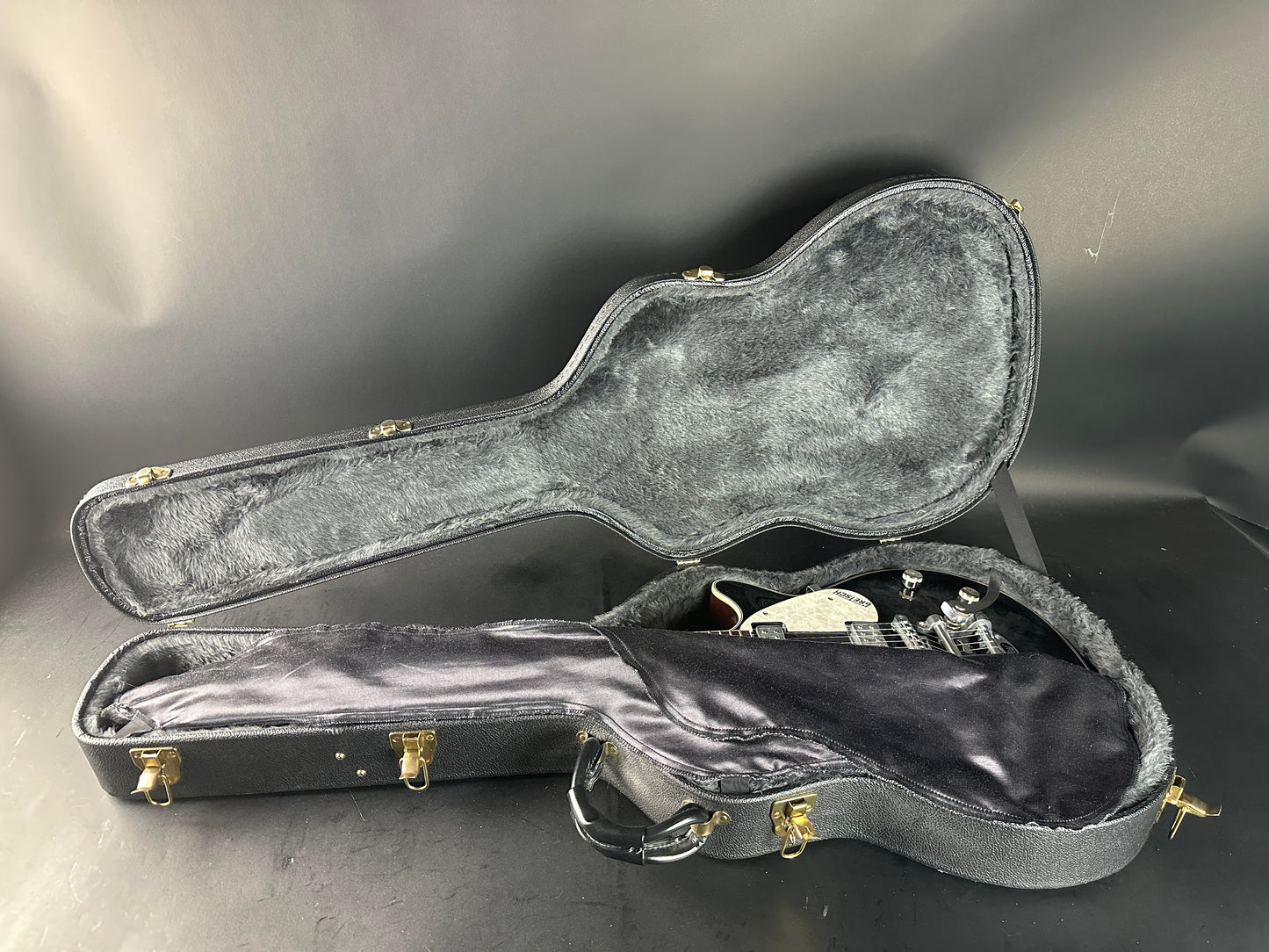 Open guitar case with a guitar inside on a gray background