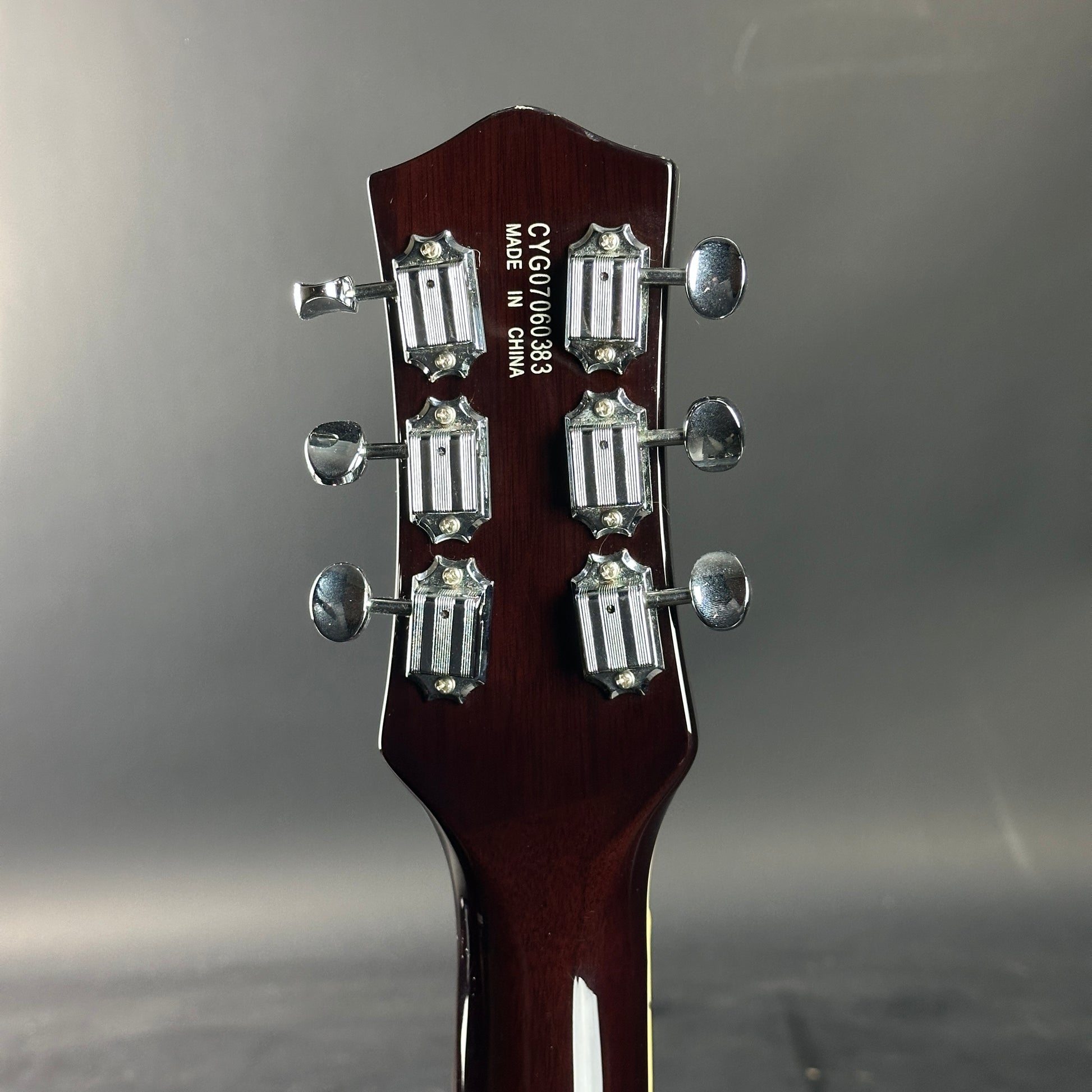Guitar headstock with tuning pegs on a gray background
