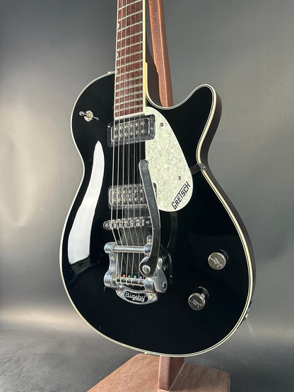 Black electric guitar with a white pickguard on a gray background