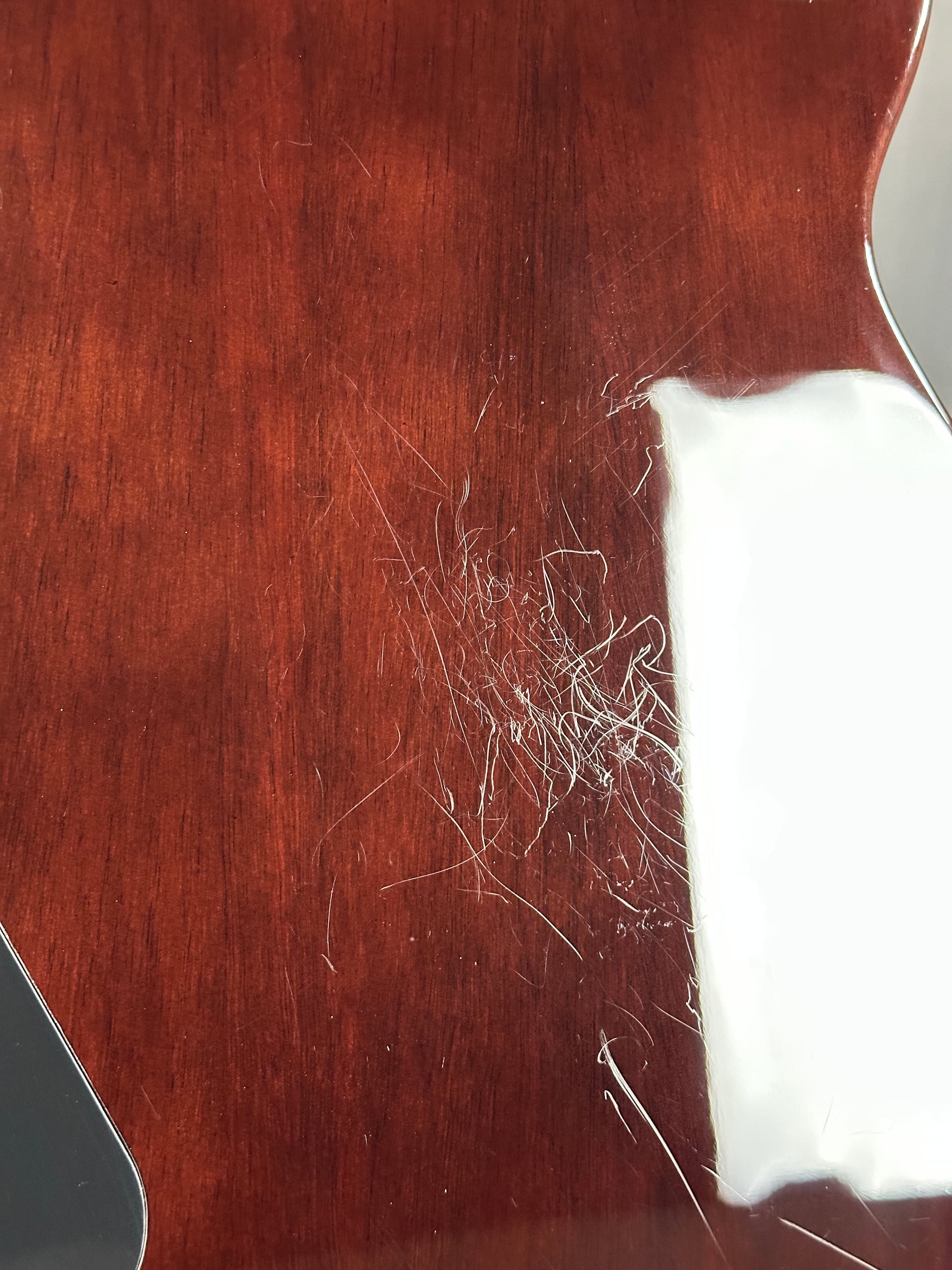 Close-up of a guitar's wooden body with visible scratches and a white cloth on top.