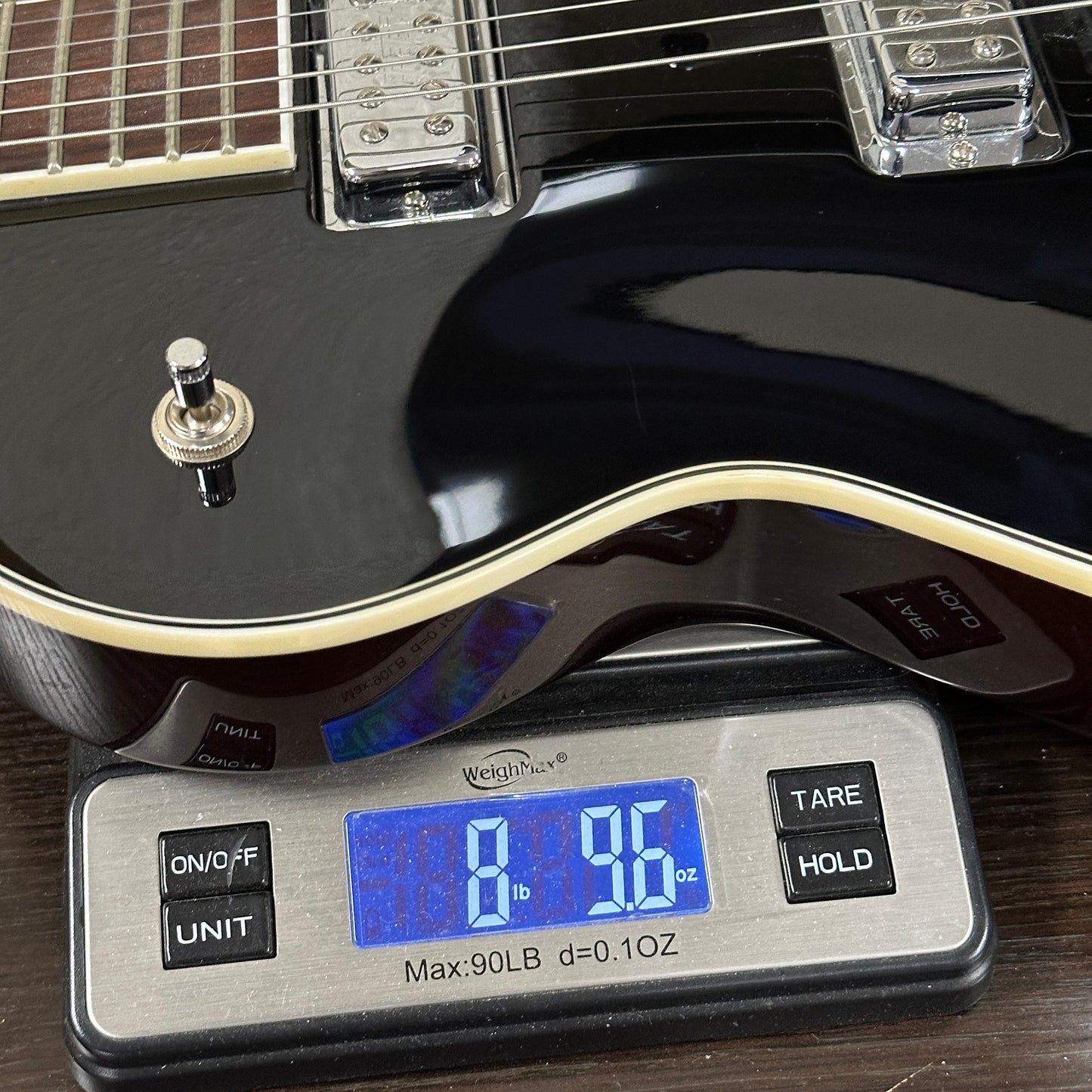 Black electric guitar on a digital scale displaying weight.