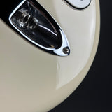 Close-up detail of a glossy cream-colored motorcycle body panel with a chrome reflector and a small silver screw fastener, set against a dark background.