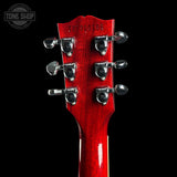 Close-up of the headstock of a red electric guitar against a black background, showing six silver tuning pegs and a Tone Shop watermark in the upper left corner.