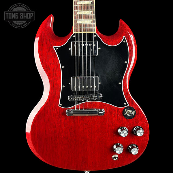 A red electric guitar with a black pickguard and chrome hardware, shown against a black background with a Tone Shop watermark in the top left corner.