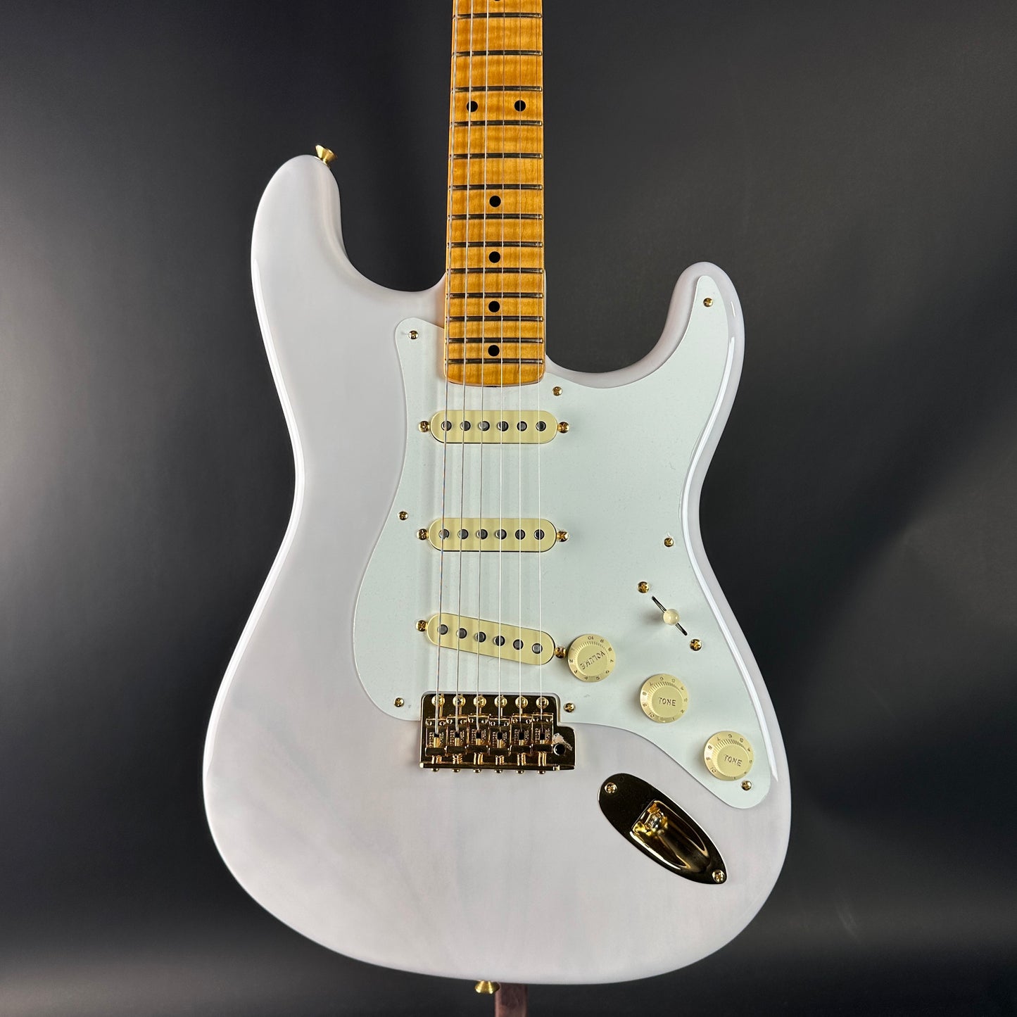 White electric guitar with a wooden fretboard on a dark background