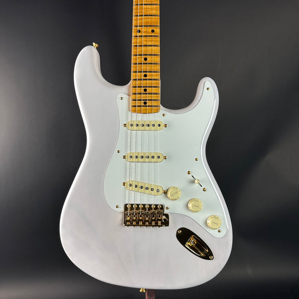 White electric guitar with a wooden fretboard on a dark background