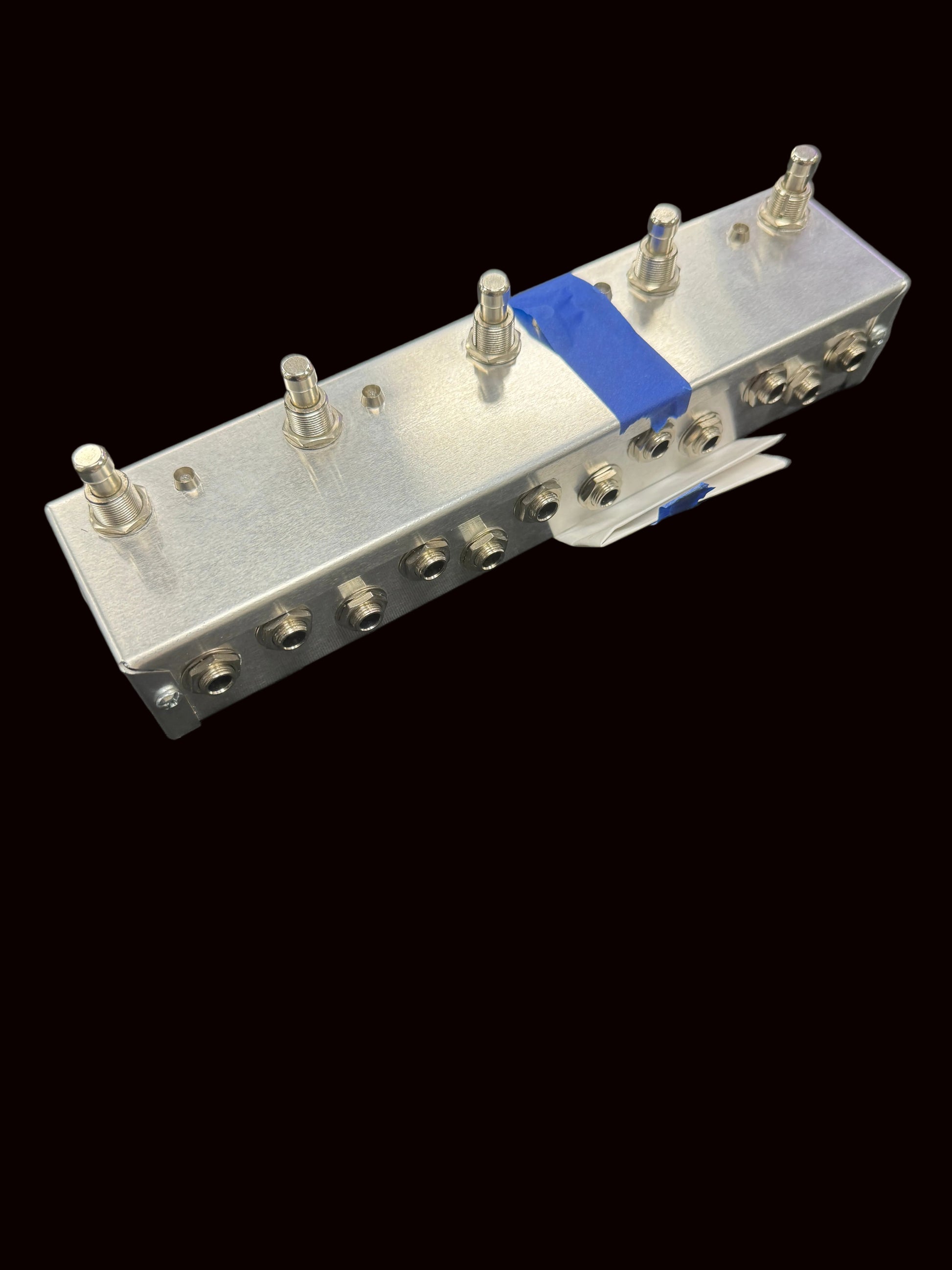 Metal component with screws and blue tape on a dark background