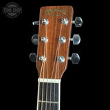 Close-up of the headstock of a Martin & Co acoustic guitar against a black background, showing the brand name in gold script and six silver tuning pegs.