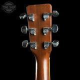 Close-up of the headstock of a guitar with a warm brown wood finish and six silver tuning pegs, shown against a solid black background with a Tone Shop watermark in the top left corner.