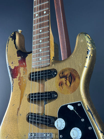 Close-up of a worn electric guitar with visible scuffs and a brand logo on a dark background.