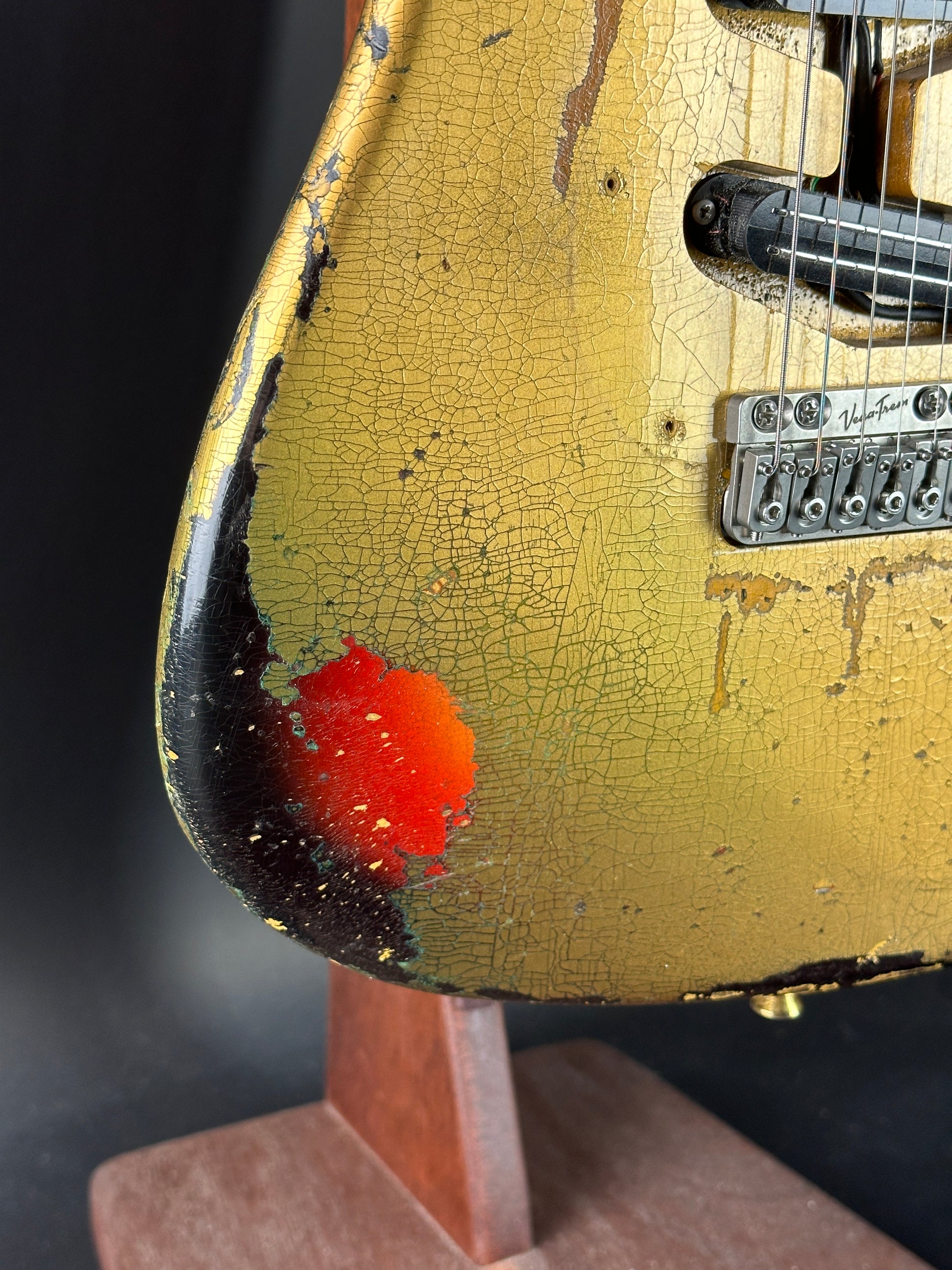 Close-up of a guitar with a cracked gold finish and red dot on a dark background