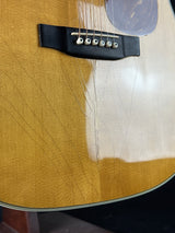 Close-up of an acoustic guitar body showing the natural wood top, bridge, strings, and part of the pickguard.