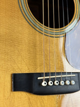 Close-up of an acoustic guitar body showing the sound hole, strings, bridge, and six white tuners against a natural wood finish.