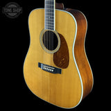 A classic acoustic guitar with a natural wood top and a dark brown sides, shown against a solid black background. A Tone Shop logo is visible in the top-left corner.
