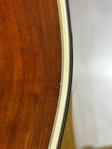 Close-up detail of an acoustic guitar body showing the rich brown wood grain of the soundboard, a cream-colored inner rim, and the edge of the black guitar neck.