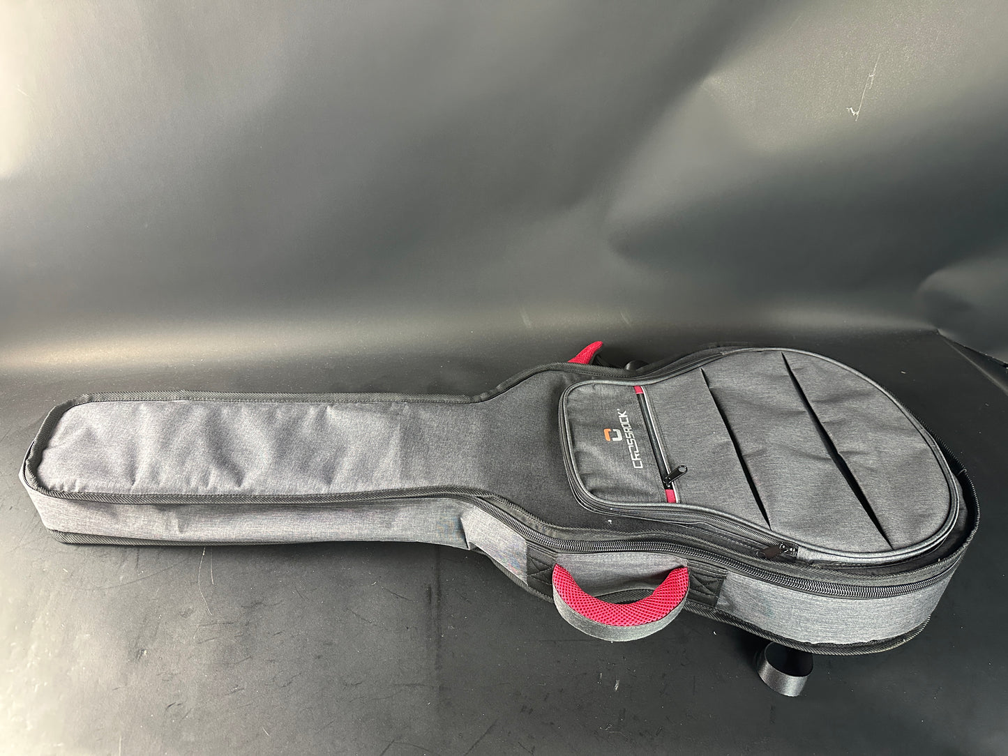 Gray guitar case with a red handle on a gray surface