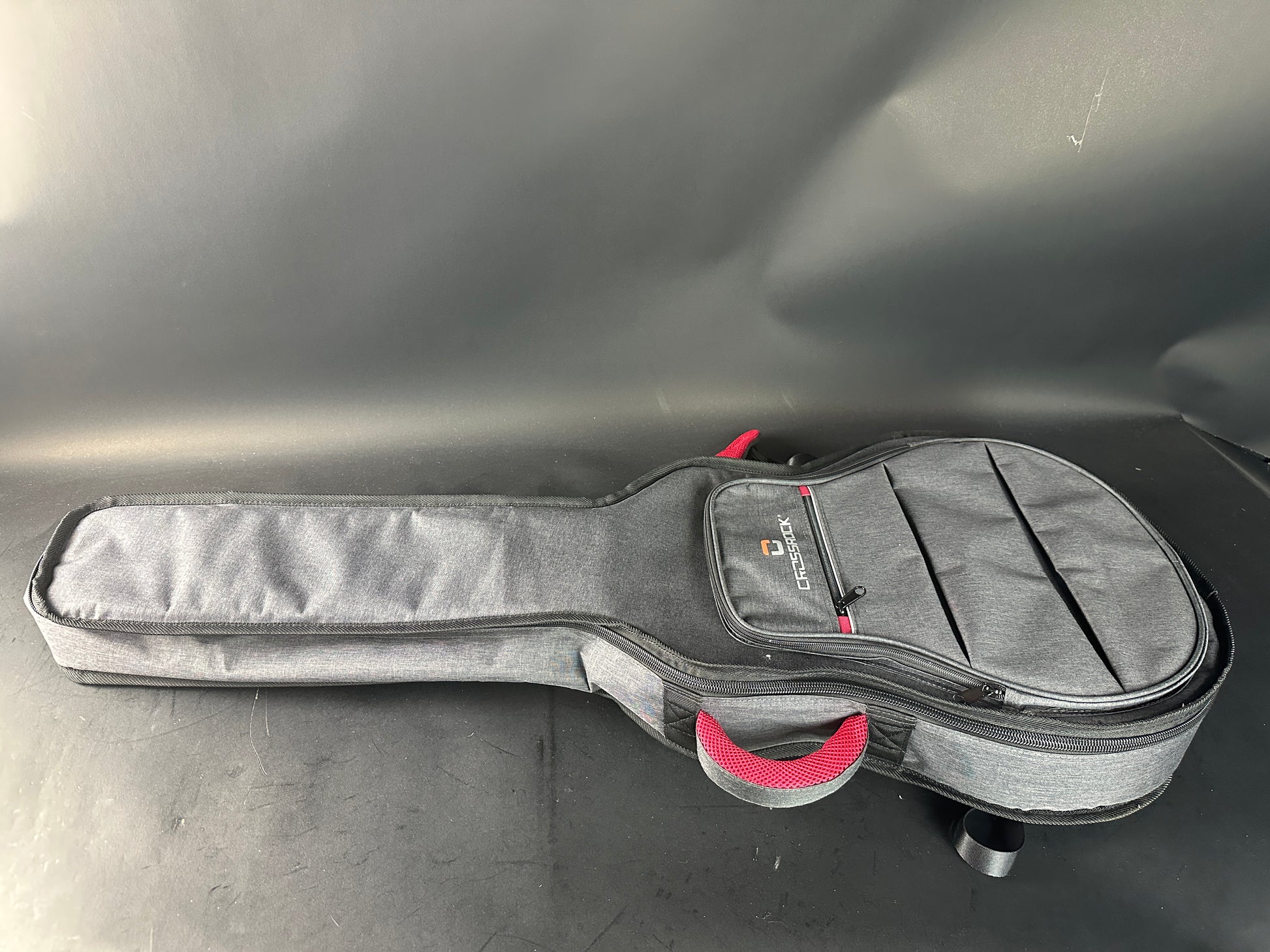 Gray guitar case with a red handle on a gray surface