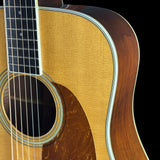 Close-up of an acoustic guitar showing the natural wood soundboard, the dark fretboard, and the curved outer edge of the body against a black background.