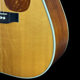 Close-up of an acoustic guitar body showing the natural wood grain, sound hole, bridge, and edge trim against a black background.