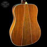The back of an acoustic guitar made of rich, warm brown wood with a glossy finish, featuring a triple-cutaway body design and a white binding edge, shown against a solid black background.