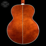 Close-up of the back of an acoustic guitar showing a rich, warm reddish-brown wood finish with a white binding edge, set against a solid black background. A Tone Shop watermark is visible in the top-left corner.