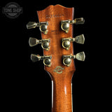 Close-up of the headstock of a Gibson 21430 acoustic guitar, showing six gold-toned tuning pegs and the Gibson logo on a black background.
