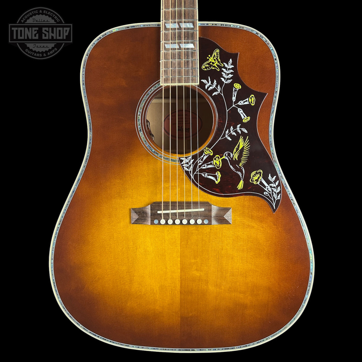A close-up of an acoustic guitar body showing a natural sunburst finish that fades to black around the edges, with a dark brown pickguard decorated with yellow birds and white floral patterns. The brand 'TONE SHOP' is visible as an overlay in the top left corner.