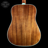 The back of an acoustic guitar with a rich, warm brown wood grain finish and a white edge trim, shown against a solid black background with a Tone Shop watermark in the top left.