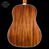 Close-up of the back of an acoustic guitar showing a rich, warm brown wood grain finish with a white edge border, set against a solid black background.