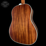 The back of an acoustic guitar with a rich, warm brown wood grain finish and white binding, shown against a solid black background.