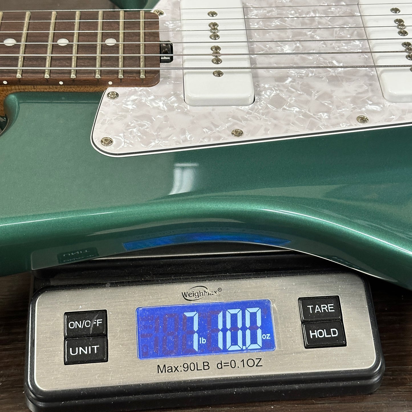 Green electric guitar on a digital scale displaying weight.