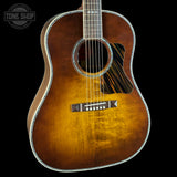 A classic acoustic guitar with a natural sunburst finish showing warm brown tones, set against a solid black background with a Tone Shop watermark in the top left corner.