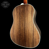 Close-up of the back of an acoustic guitar showing a rich wood grain finish, with a white binding edge and a visible Tone Shop watermark in the top left corner.