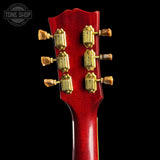 Close-up of the headstock of an electric guitar with a glossy red finish and gold tuning pegs, shown against a solid black background. A 'TONE SHOP' watermark is visible in the top left corner.