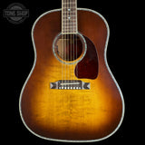 A classic acoustic guitar with a natural sunburst finish, featuring a warm golden-yellow center fading to dark brown at the edges, set against a solid black background.