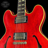 Close-up of a red electric guitar body with gold binding, black pickups, and a black background. A Tone Shop watermark is visible in the top left corner.