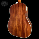 Close-up of the back of an acoustic guitar showing a rich, warm brown wood grain finish with white binding, set against a solid black background.
